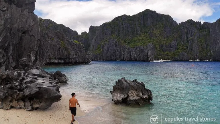 man walking at the beach with towering limestone cliffs and different hues of blue water on a summer day in El nido, Palawan, Philippines
