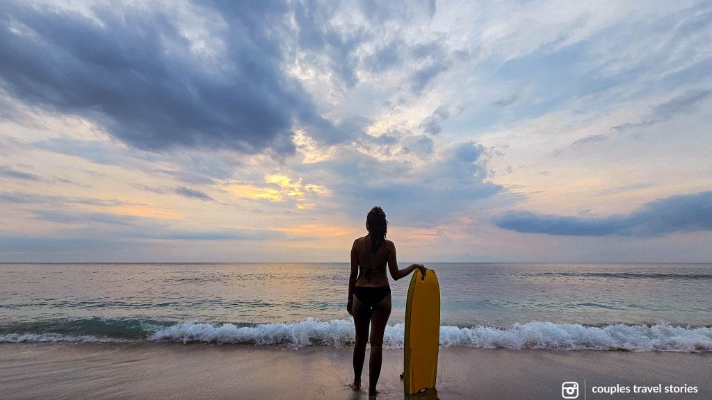 Standing at the coast with the surf board at sunset after surfing in Senggigi, Lombok